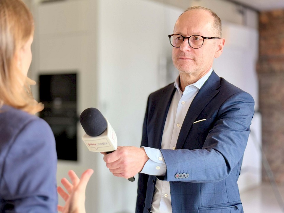 Ein Mann im Anzug hält ein Mikrofon und interviewt eine Frau in einem professionellen Setting während eines Medientrainings.